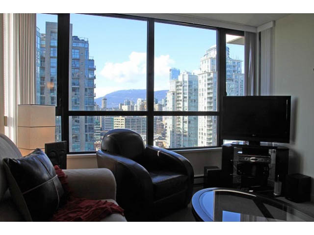 Living room with large windows offering a stunning city view, modern furnishings, and a sleek coffee table.