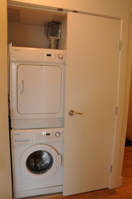 Bright laundry room with stacked washer and dryer, white door, hardwood floors. - 1405- 565 Smithe Street, Vancouver Downtown