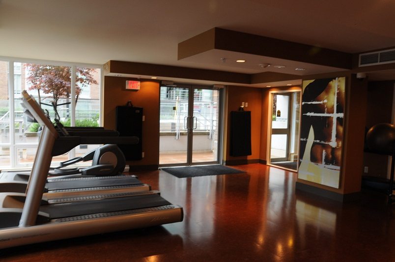 Bright and modern fitness room with treadmills and large windows, showcasing a city view. - 1405- 565 Smithe Street, Vancouver Downtown