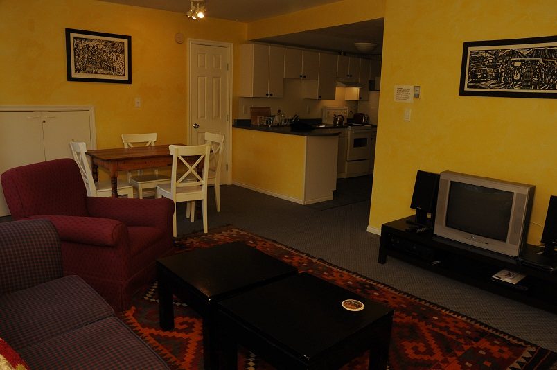 Living room with yellow walls, coffee table, and kitchen in the background. - 2018 Rivergrove Place, North Vancouver