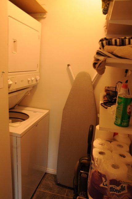 Small laundry room with stacked washer and dryer, ironing board, and shelves. - 2018 Rivergrove Place, North Vancouver