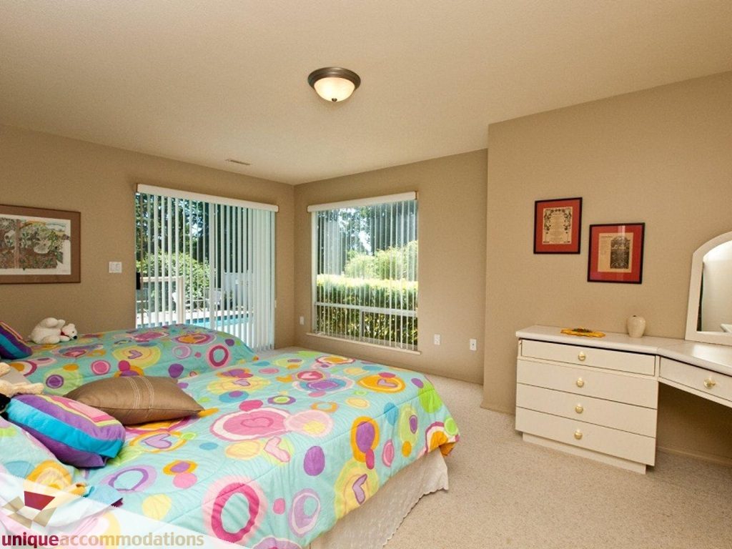 Bright bedroom with colorful bedding and large windows, featuring a dresser and mirror. - 750 Anderson Crescent, West Vancouver