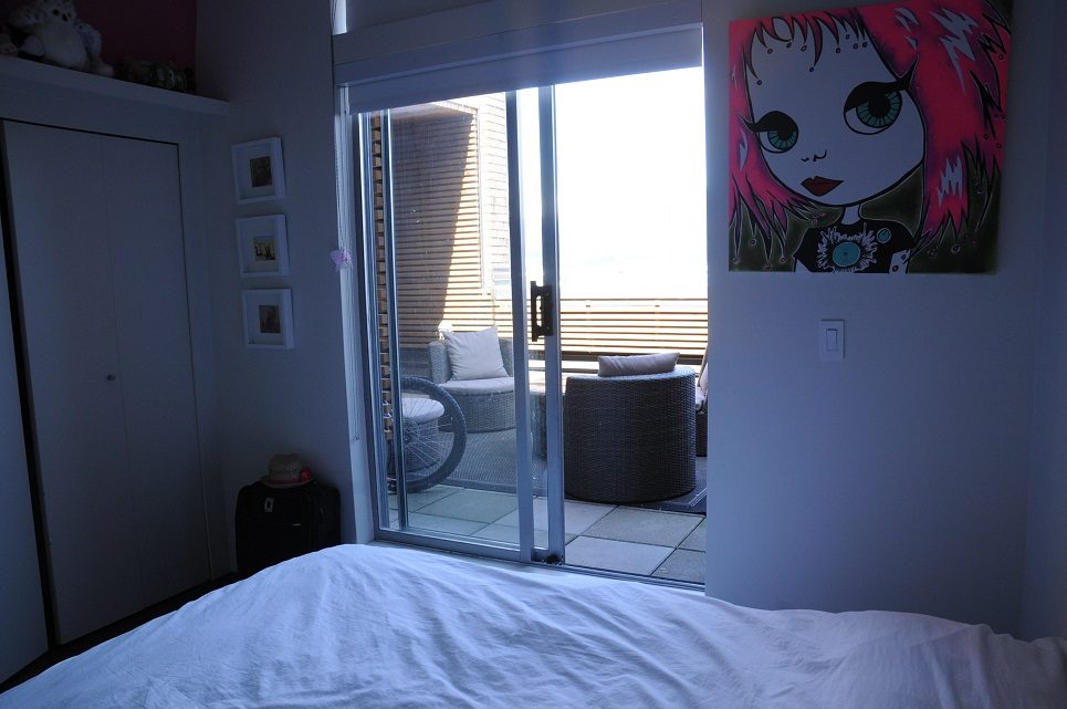 Bright bedroom with large glass door leading to a balcony, featuring a vibrant artwork of a girl with red hair.
