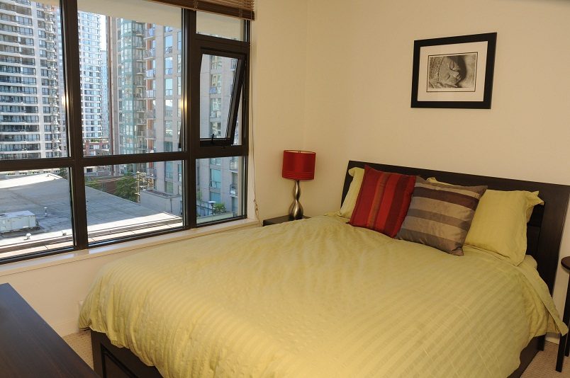 Furnished bedroom with city view, red lamp, and striped pillows. - 705 - 538 Smithe, Vancouver Downtown
