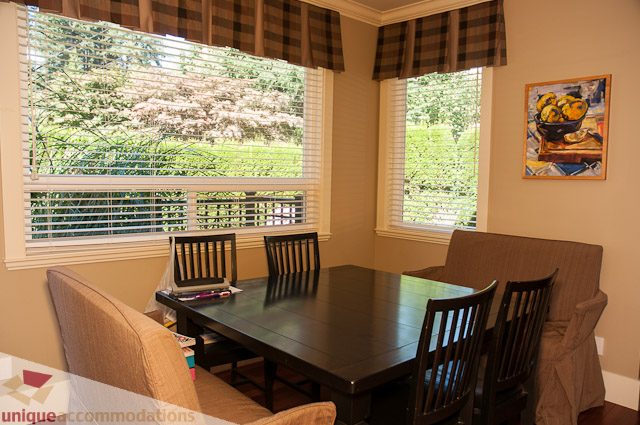 Bright dining area with large windows, checkered valances, and a fruit painting on the wall. - 3035 Newmarket Drive, North Vancouver