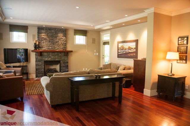 Spacious living room with hardwood floors, stone fireplace, and large windows. - 3035 Newmarket Drive, North Vancouver