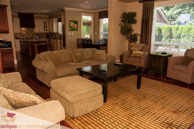 Furnished living room with hardwood floors, large windows, and a cozy sectional sofa. - 3035 Newmarket Drive, North Vancouver