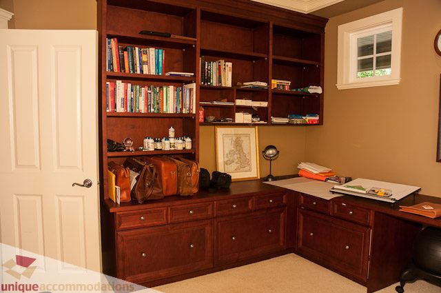 Furnished home office with wooden shelves, desk, and framed artwork. - 3035 Newmarket Drive, North Vancouver