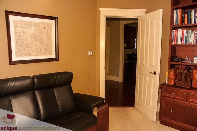 Living room with leather couch and framed map, leading to a kitchen area. - 3035 Newmarket Drive, North Vancouver