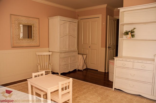 Bright bedroom with white furniture and wooden floors, featuring a large armoire and a dresser. - 3035 Newmarket Drive, North Vancouver