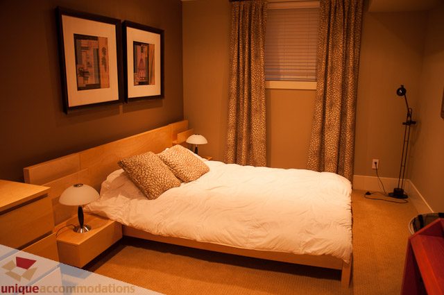 Furnished bedroom with a cozy bed, leopard print curtains, and a bedside lamp. - 3035 Newmarket Drive, North Vancouver