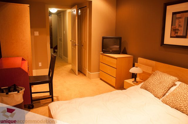 Furnished bedroom with a bed, nightstand, and TV; warm lighting. - 3035 Newmarket Drive, North Vancouver