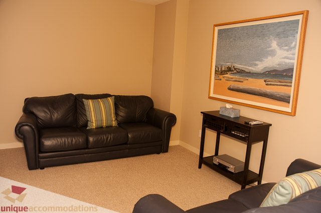 Furnished living room with black leather couch and beach painting. - 3035 Newmarket Drive, North Vancouver