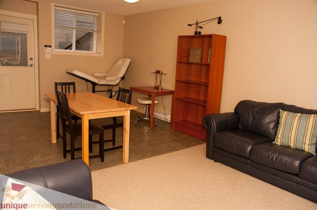 Living room with black leather couch, wooden dining table, and bookshelf. - 3035 Newmarket Drive, North Vancouver