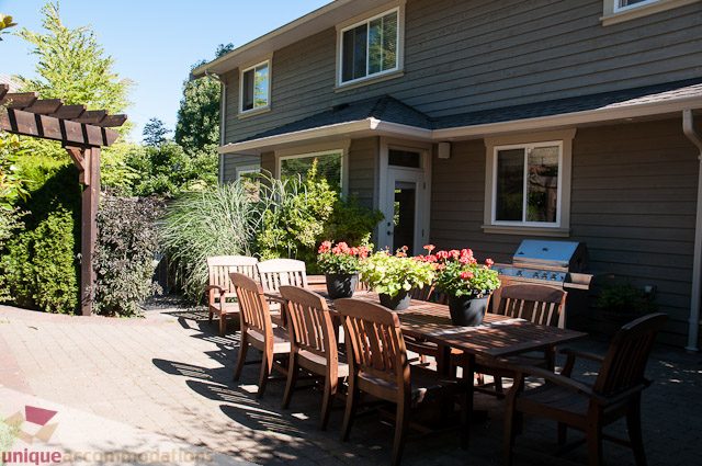 Furnished patio with wooden furniture and potted plants, surrounded by greenery. - 3035 Newmarket Drive, North Vancouver