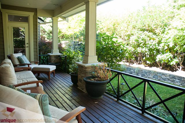 Furnished patio with wooden furniture, stone wall, and lush greenery. - 3035 Newmarket Drive, North Vancouver