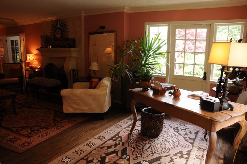 Formal living room with hardwood floors, patterned rugs, and a large window showing greenery. - Main House - 440 Stevens Drive, West Vancouver