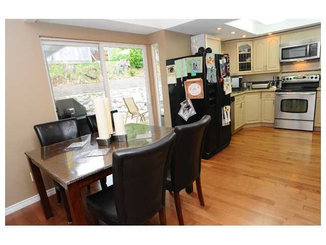 Bright kitchen with hardwood floors and a dining area featuring a black table and chairs, near a large window offering a...