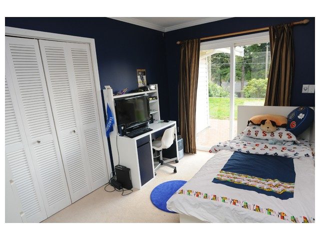 Bright bedroom with louvered closet doors, colorful bedding, and a view of the backyard. - 1889  Alderlynn Drive, North Vancouver