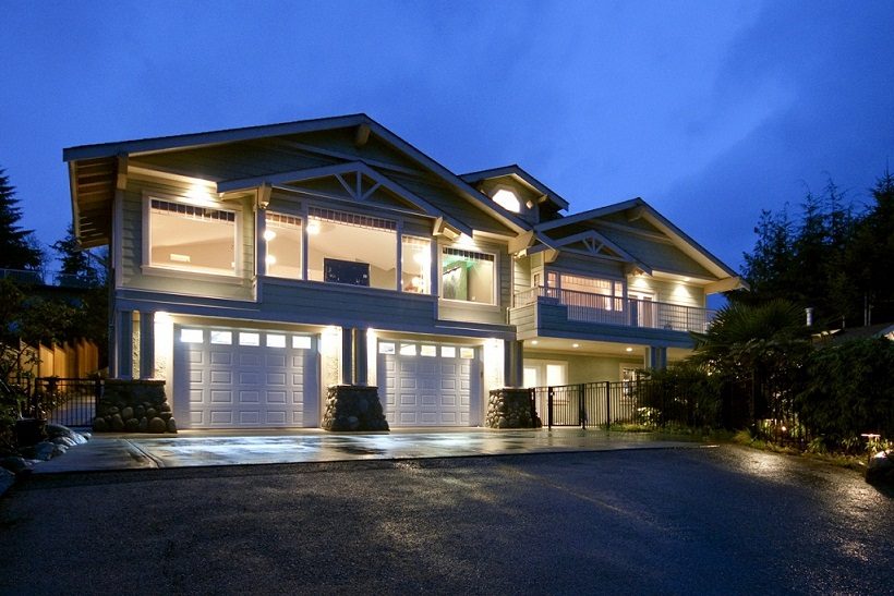 Bright 7-bedroom house with illuminated garage and balcony at dusk. - 967 Roslyn Blvd., North Vancouver