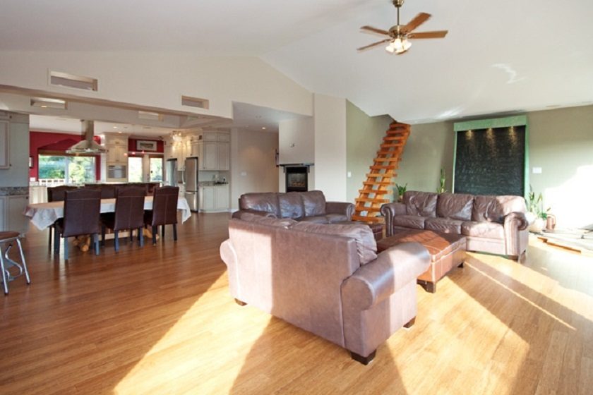 Open-concept living room with hardwood floors, leather furniture, and a kitchen in the background. - 967 Roslyn Blvd., North Vancouver
