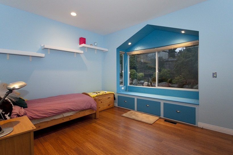 Bright bedroom with hardwood floors, blue accent wall, and a window view of greenery. - 967 Roslyn Blvd., North Vancouver