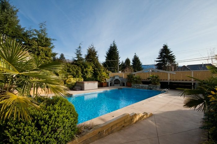 Spacious outdoor pool area with palm trees and a wooden deck. - 967 Roslyn Blvd., North Vancouver
