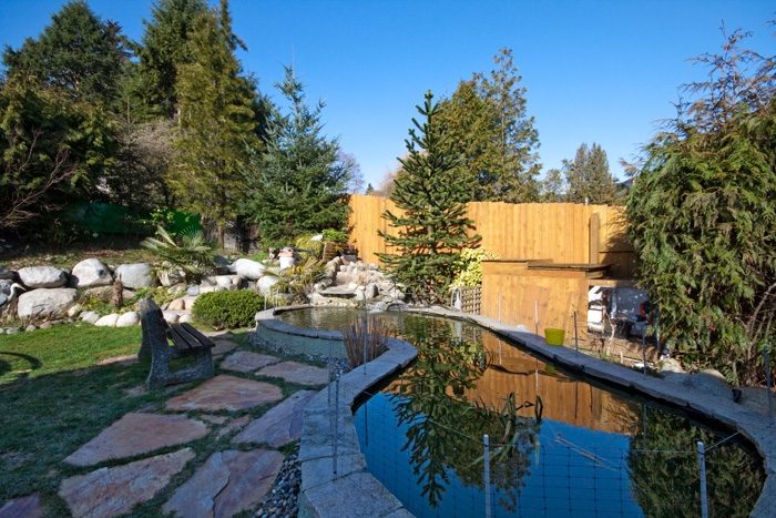 Spacious backyard with stone pathways, wooden deck, and a serene pond reflecting the surrounding trees. - 967 Roslyn Blvd., North Vancouver