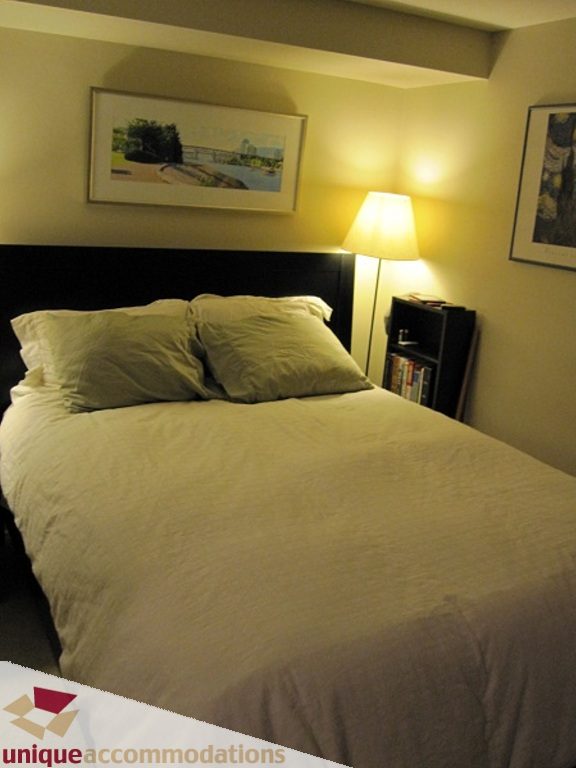 Furnished bedroom with a neatly made bed, lamp, and framed artwork. - 6-1250 West 6th Ave, Vancouver West Side