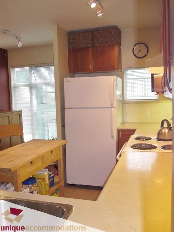 Bright kitchen with light wood countertops and a white refrigerator, featuring a clock on the wall and a window with blinds.