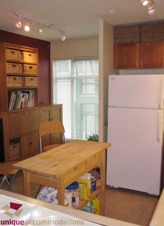 Bright kitchen with wooden cabinets, white refrigerator, and a small dining area with a wooden table and chair.