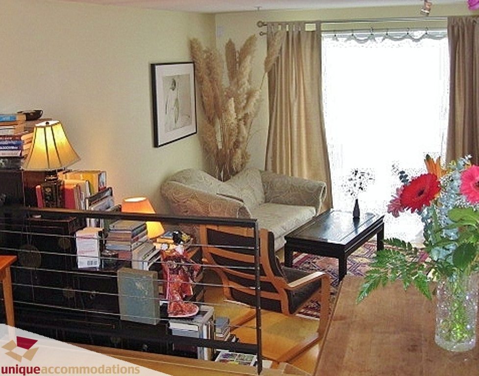 Bright living room with hardwood floors, cozy seating, and a large window with curtains. - 306-3727 West 10th Ave, Vancouver West Side