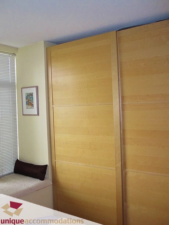 Bright bedroom with wooden sliding doors and a small window with blinds. - 306-3727 West 10th Ave, Vancouver West Side