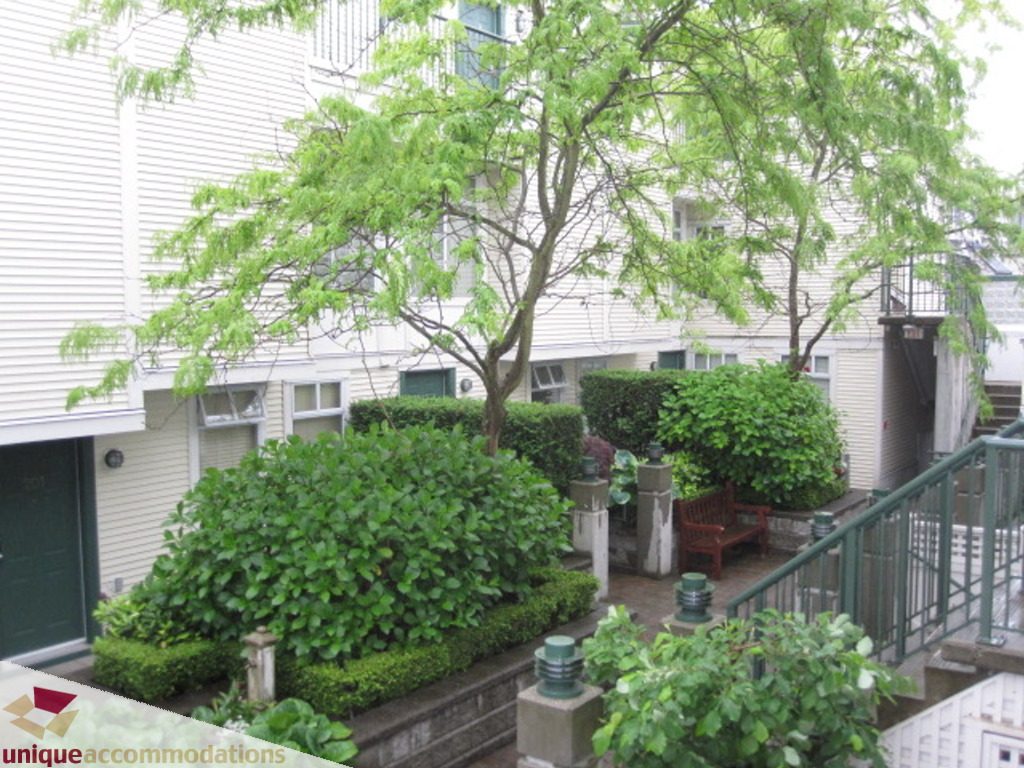 Furnished patio with lush greenery and a red bench, steps leading up. - 306-3727 West 10th Ave, Vancouver West Side