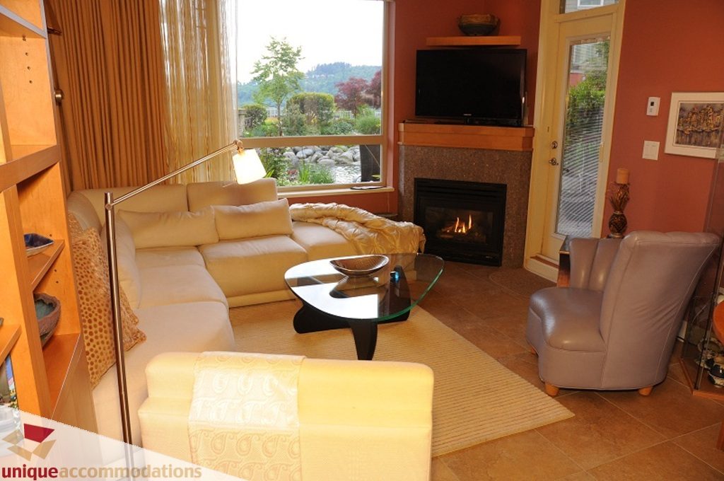 Bright living room with fireplace, large window, and cozy furniture. - 103-580 Raven Woods Drive, North Vancouver