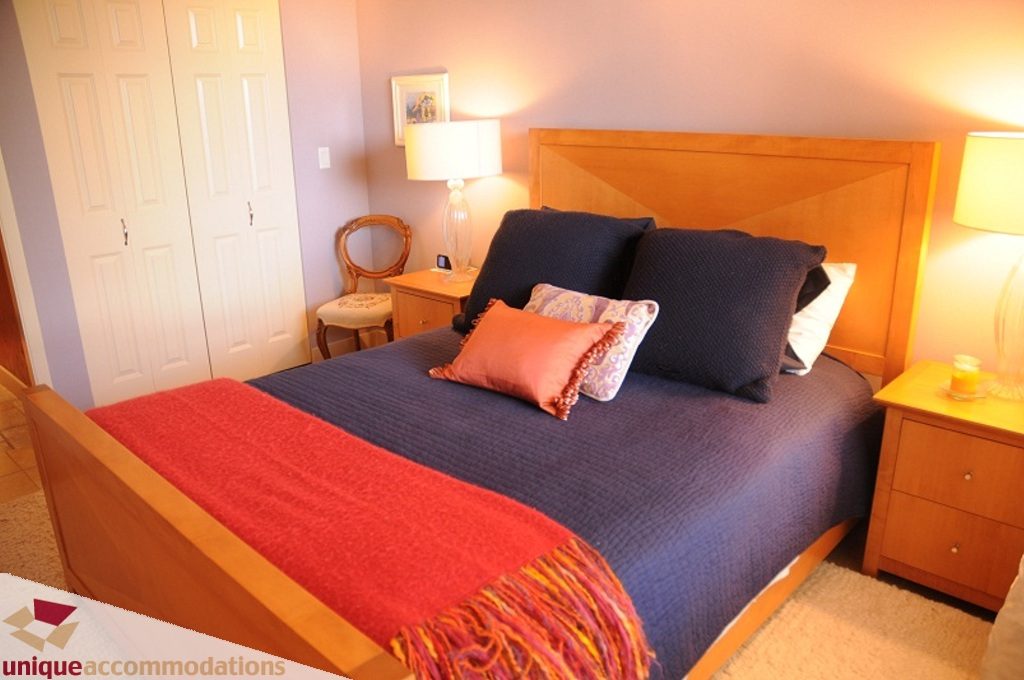 Furnished 2-bedroom condo with two twin beds, wooden headboards, and cozy bedding. - 103-580 Raven Woods Drive, North Vancouver