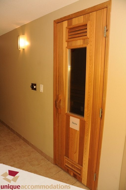 Furnished hallway with wooden door and wall sconce. - 103-580 Raven Woods Drive, North Vancouver