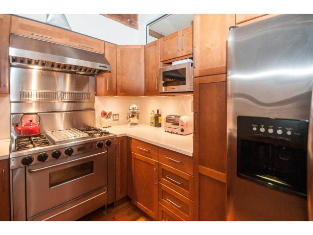 Bright kitchen with stainless steel appliances, wooden cabinets, and a red kettle on the stove. - 410 - 550 Beatty Street, Vancouver Downtown