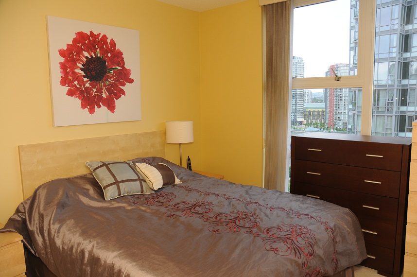 Bright bedroom with city view and large window, modern furnishings, and vibrant red flower artwork.