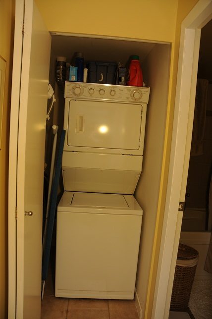 Bright laundry room with stacked washer and dryer, neatly organized with cleaning supplies. - 1501 -1077 Marinaside Crescent, Vancouver Downtown