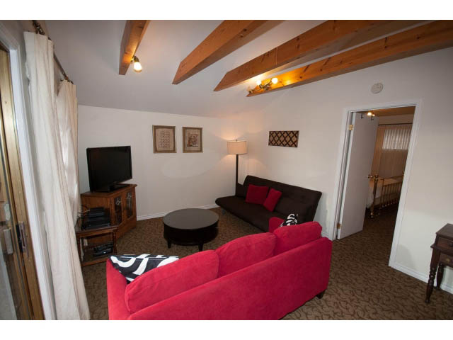 Furnished living room with red sofa, wooden beams, and a view of another room. - Cottage - Sinclair Street, West Vancouver