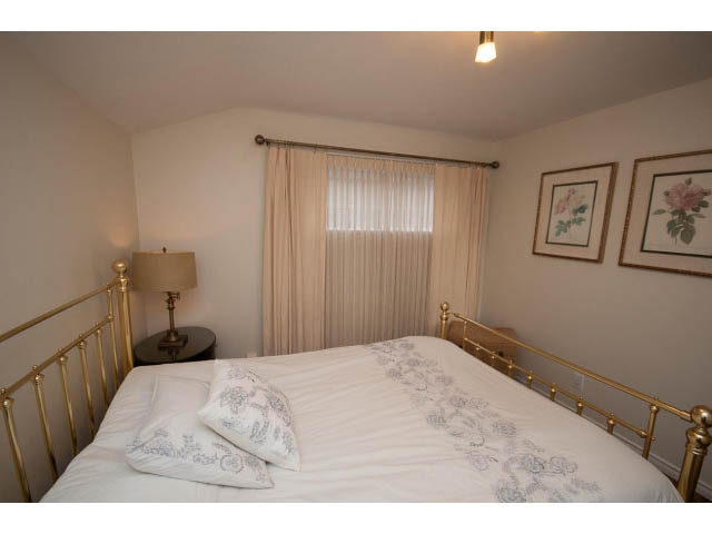 Bright bedroom with gold railings, floral bedding, and framed artwork. - Cottage - Sinclair Street, West Vancouver