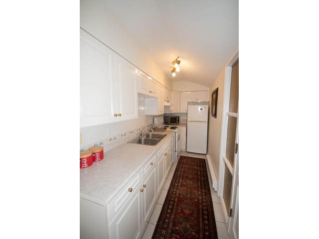 Bright kitchen with white cabinets, granite countertops, and a red rug. - Cottage - Sinclair Street, West Vancouver