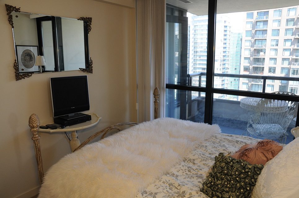 Bright bedroom with city view and cozy bedding, featuring a desk and large mirror. - 2605 - 928 Homer Street, Vancouver Downtown