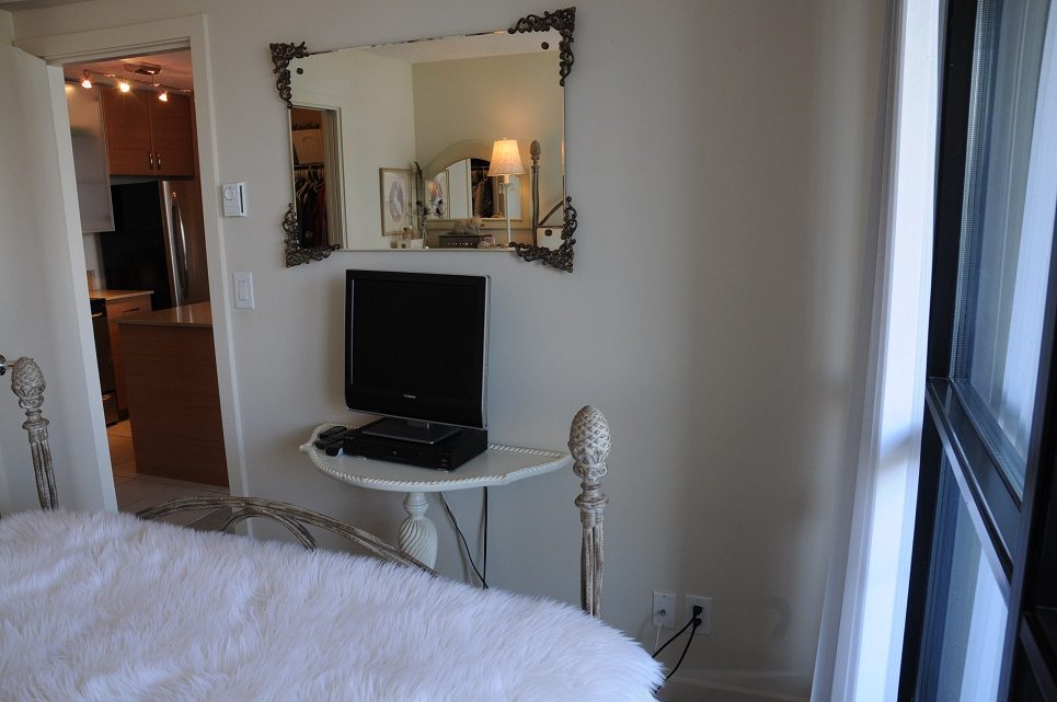 Bright bedroom with a fluffy white bedspread and a large mirror above a flat-screen TV, overlooking the city.