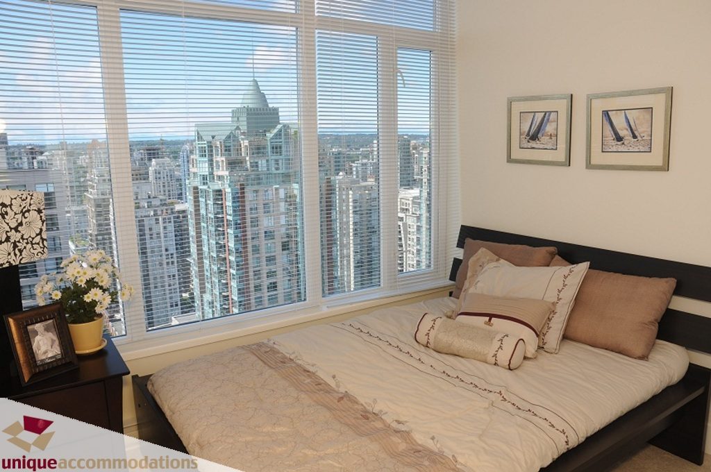 Furnished bedroom with city view and large windows, featuring a comfortable bed and modern decor. - 3401 - 888 Homer Street, Vancouver Downtown