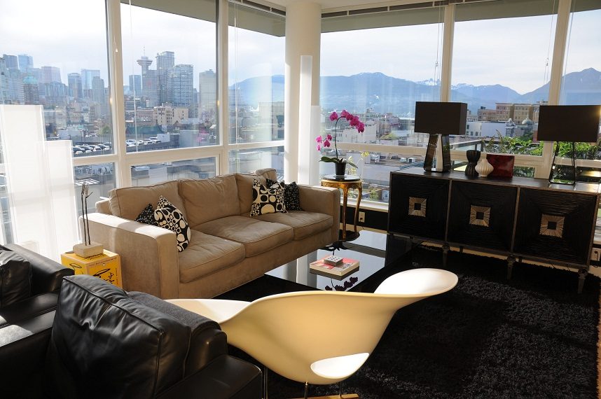 Bright living room with city view and modern decor, featuring a tan sofa and black leather armchair. - 903-718 Main Street, Vancouver Downtown