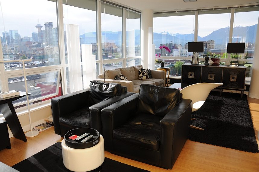Bright living room with city view, black leather furniture, hardwood floors, and modern decor. - 903-718 Main Street, Vancouver Downtown
