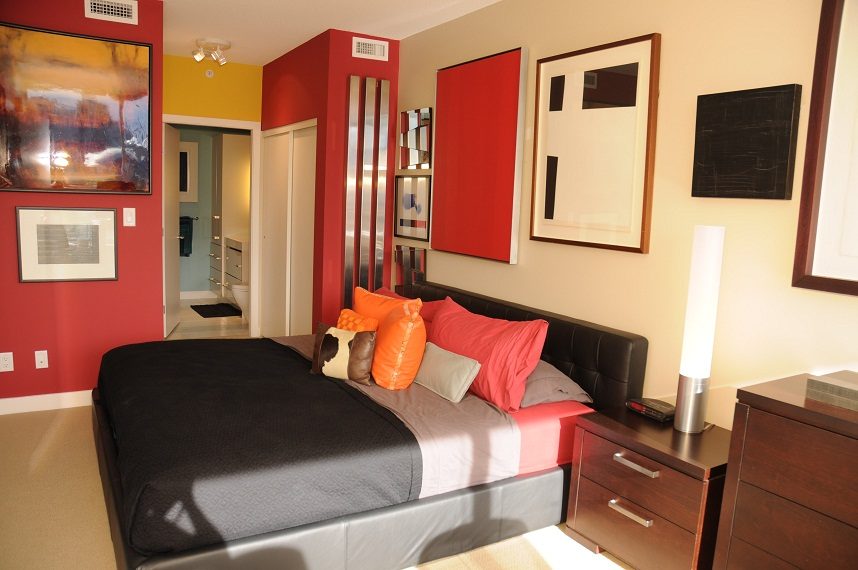 Furnished bedroom with vibrant red walls, modern artwork, and a black leather bed. - 903-718 Main Street, Vancouver Downtown
