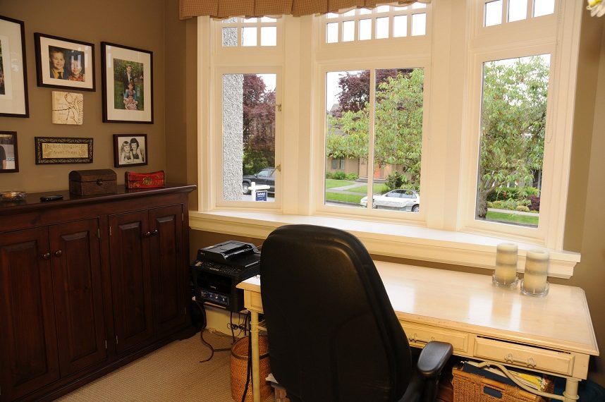 Bright home office with large windows, wooden desk, and family photos on the wall. - 4069 West 37th Ave, Vancouver West Side